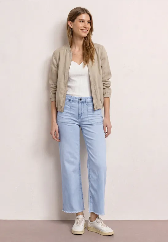 Femme en chemisier blanc, bomber beige, jean large bleu clair et baskets claires.