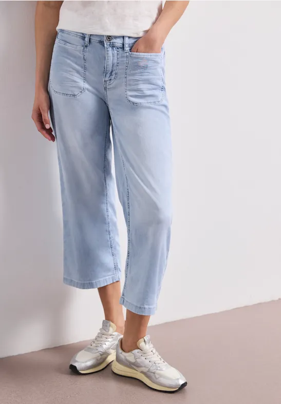 Lichtblauwe wijde cropped jeans gecombineerd met zilverkleurige sneakers.
