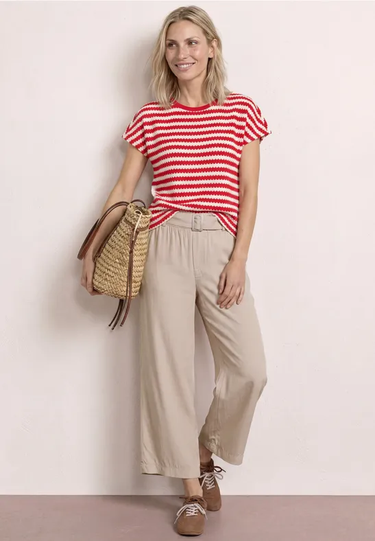 Vrouw in rood-wit gestreept shirt, beige wijde broek en strozak