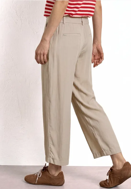 Persoon in beige stofbroek, bruine veterschoenen en rood-wit gestreept shirt voor witte achtergrond.