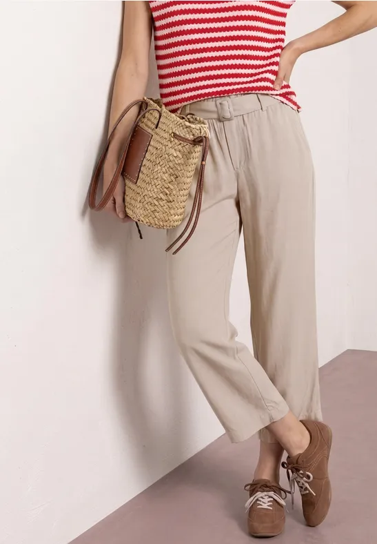 Beige broek met elastische taille, rood-wit gestreept shirt, bruine suède schoenen met strik en gevlochten tas.