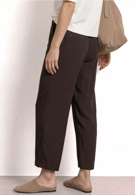 Vue latérale d'une personne portant un pantalon marron foncé ample, des mocassins beiges et un sac assorti.