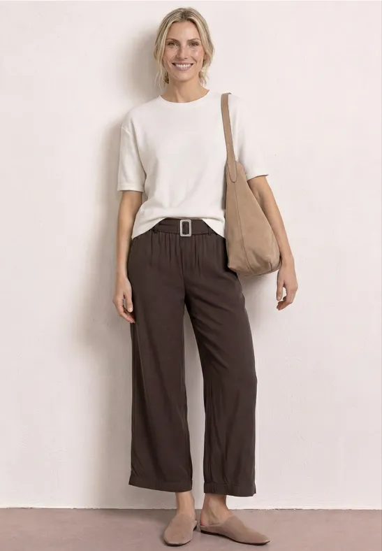 Femme en t-shirt blanc, pantalon marron ample, sac en bandoulière beige et chaussures plates.