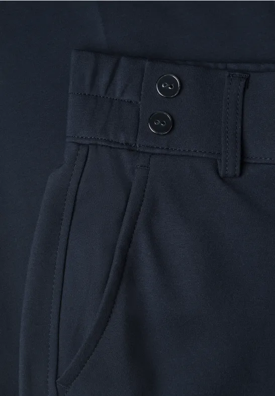 Close-up van een donkerblauwe broek met twee knopen, riemlussen en zijzak.