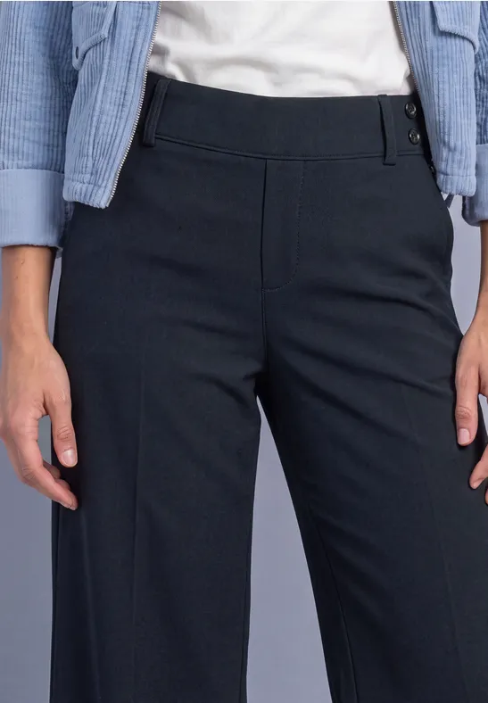 Vrouw draagt recht gesneden donkerblauwe broek met hoge taille, wit shirt en lichtblauw jasje.