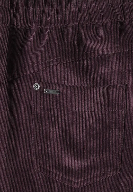 Close-up van een paarse corduroybroek met zakje en metalen label.