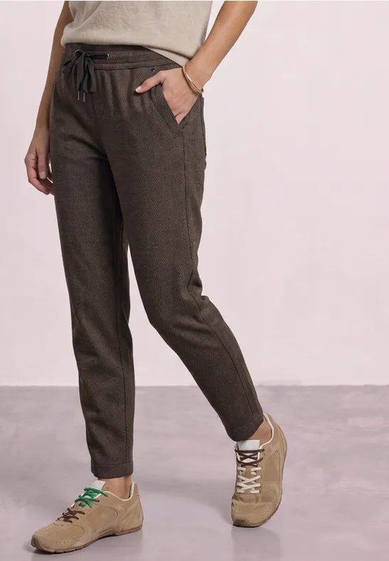 Donkerbruine linnen broek met verstelbaar koord, smalle pasvorm en zijzakken, gecombineerd met beige sneakers.