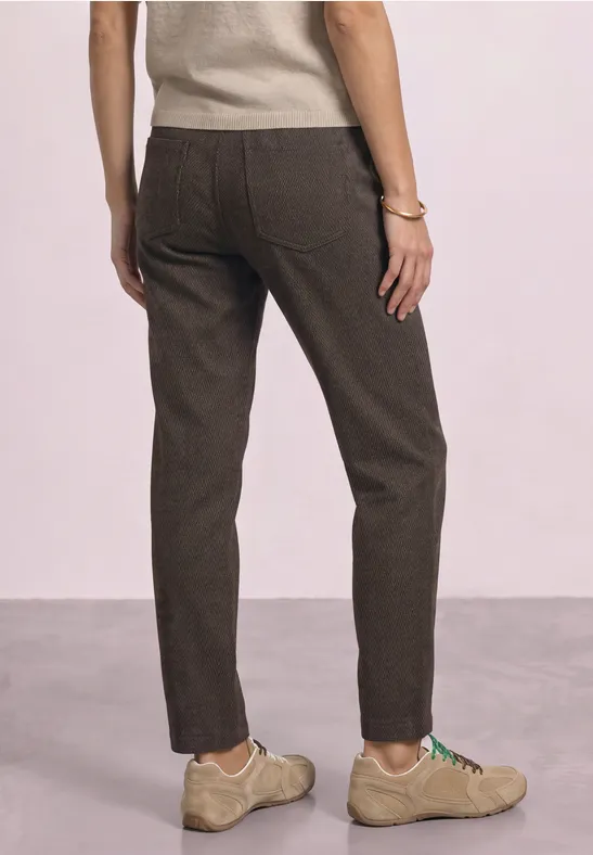 Persoon van achteren in bruine broek en beige schoenen voor een neutrale achtergrond.
