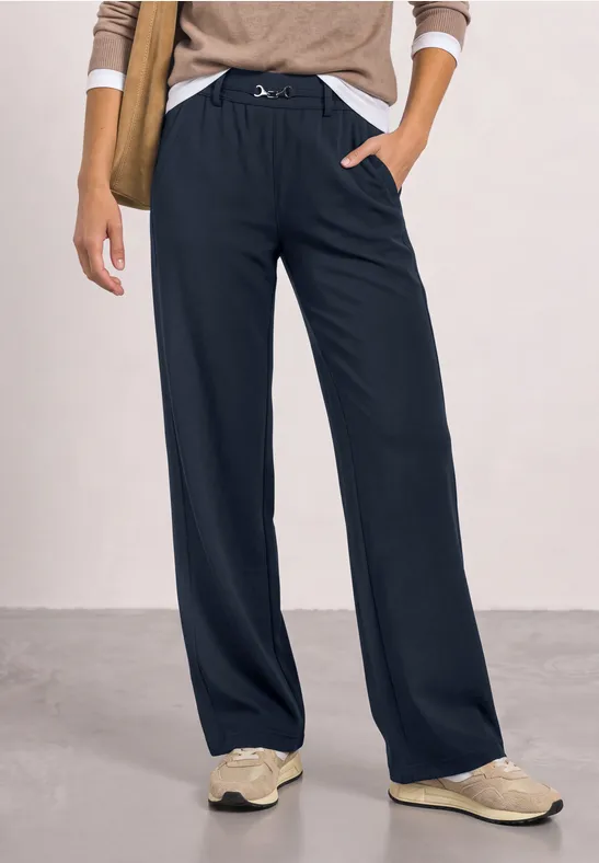 Frau trägt weite, schwarze Hose mit Tunnelzug und beigefarbene Sneaker.