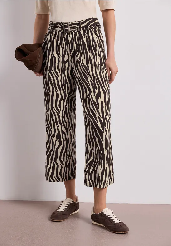Pantalon court imprimé zèbre, haut blanc, pochette et baskets marron.