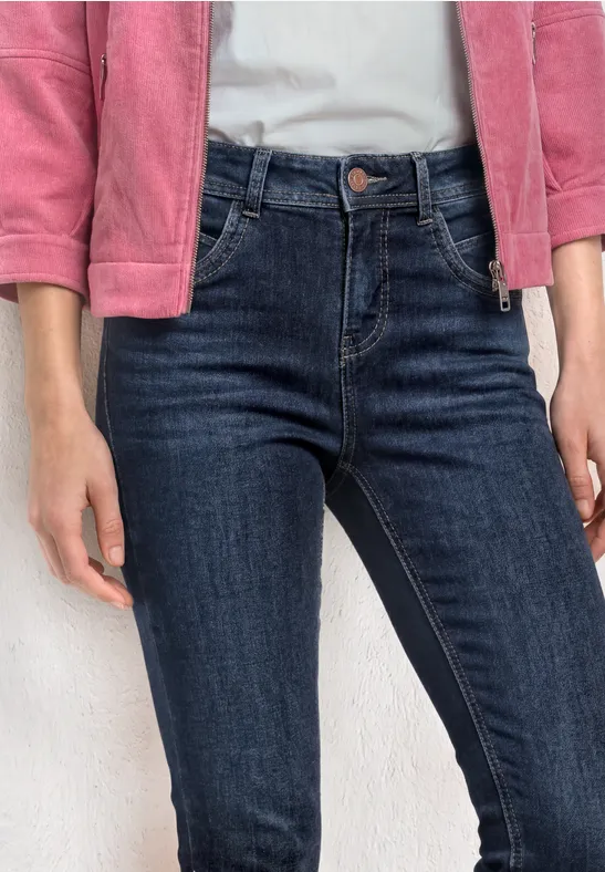 Iemand draagt een donkerblauwe spijkerbroek en een roze jas, handen langs het lichaam.