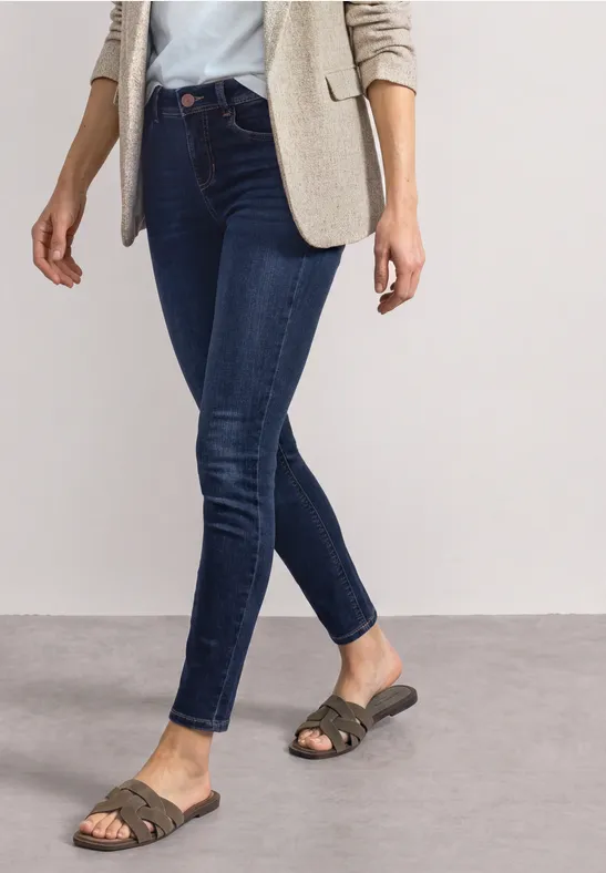 Une personne porte un blazer beige, un chemisier blanc, un jean skinny bleu et des sandales tressées.
