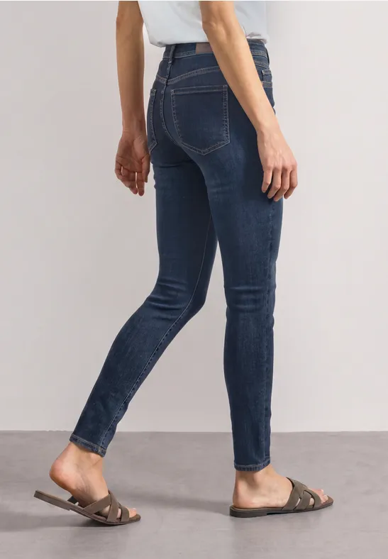 Jeans skinny bleu foncé et sandales marron plates portées par une femme.