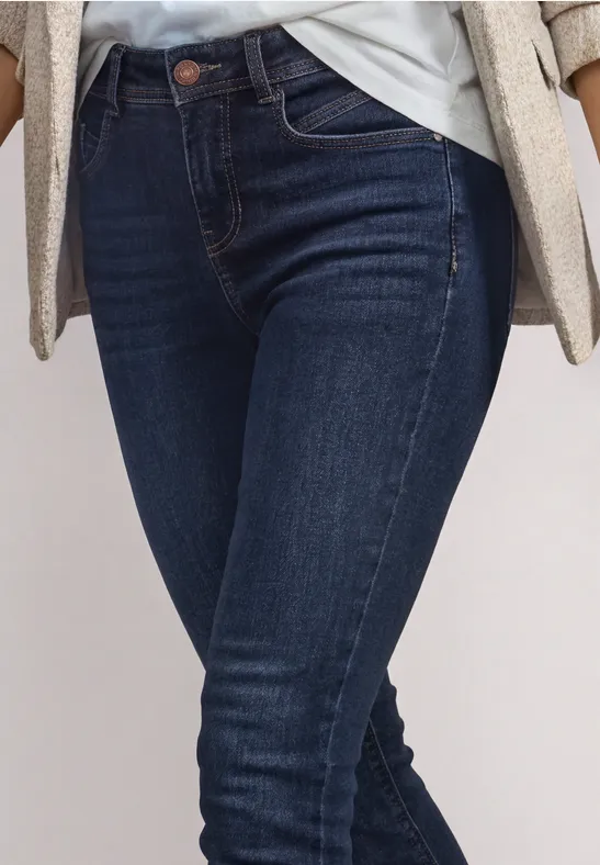Femme portant un jean skinny bleu foncé, t-shirt blanc et blazer beige, vue sur taille et jambes.