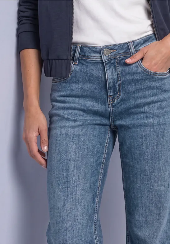 Femme en jean bleu, t-shirt blanc et veste sombre, main dans la poche