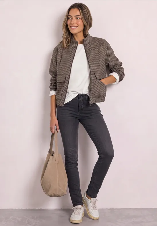 Femme en bomber, t-shirt blanc, jean noir, baskets blanches, tenant un sac beige.