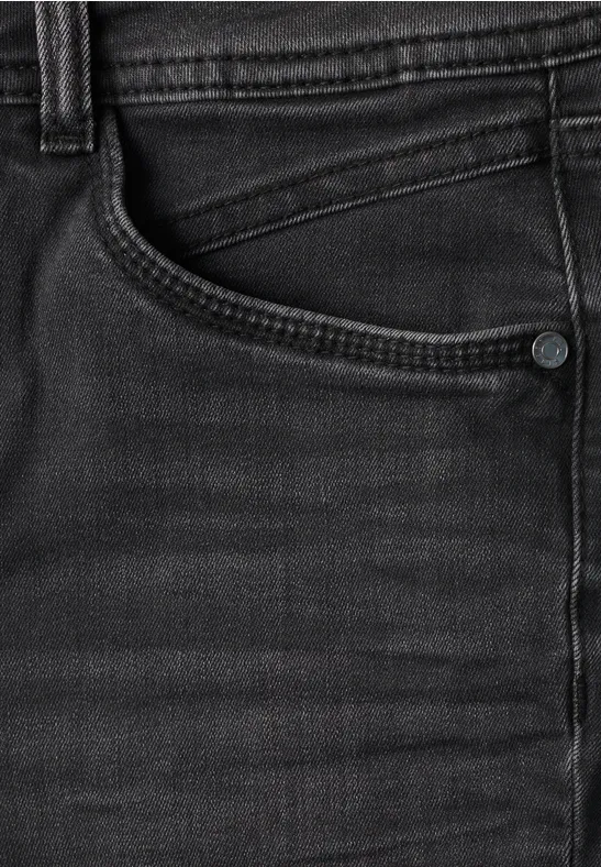 Gros plan d’un jean noir avec poche et coutures apparentes.