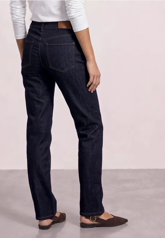 Achteraanzicht van persoon met donkere, rechte jeans en bruine ballerina's.