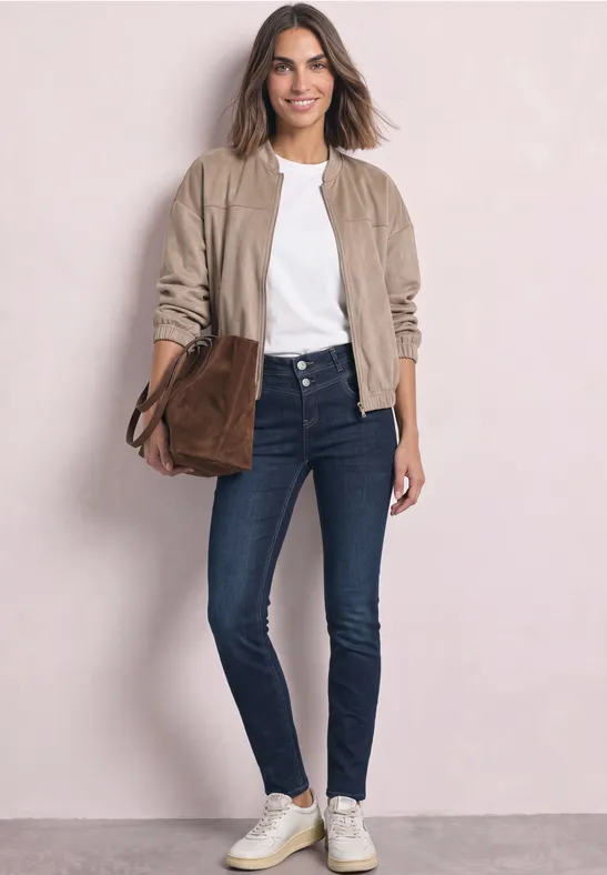 Femme élégante en jean, t-shirt blanc, blouson beige, baskets blanches et sac marron sur fond clair.