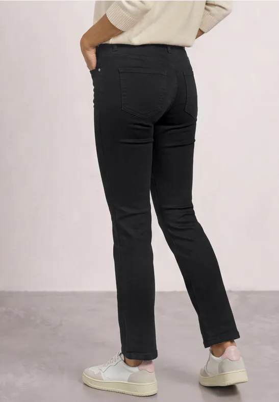 Vue arrière d’une personne portant un jean noir slim et des baskets blanches sur fond clair.