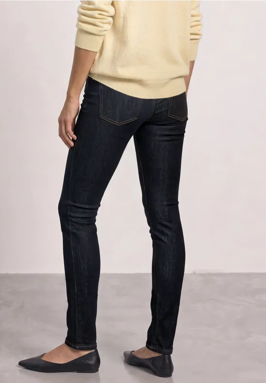 Person steht von hinten in dunklen Skinny-Jeans, beigem Pullover und flachen Ballerinas.