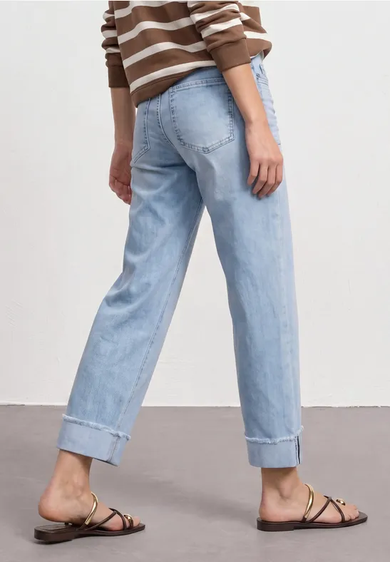 Persoon draagt lichtblauwe omgeslagen jeans, gestreepte trui en platte sandalen.