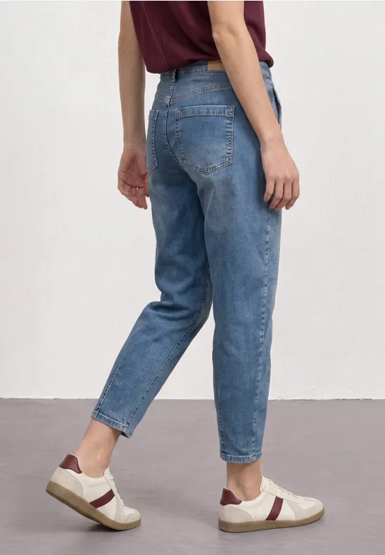 Persoon van achteren in losse blauwe jeans en sneakers voor een witte achtergrond.