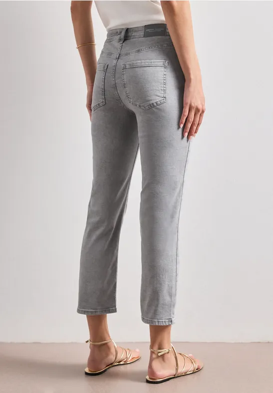 Achteraanzicht van een persoon in grijze, hooggetailleerde jeans tot op de enkel, recht model met platte sandalen.