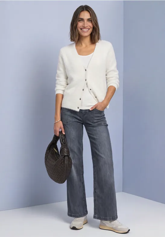 Femme portant un gilet blanc, jean gris, baskets et sac panier rond.