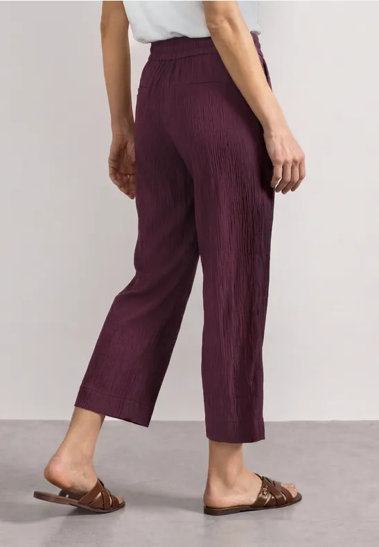 Achteraanzicht van een persoon in paarse geplooide broek en bruine sandalen.