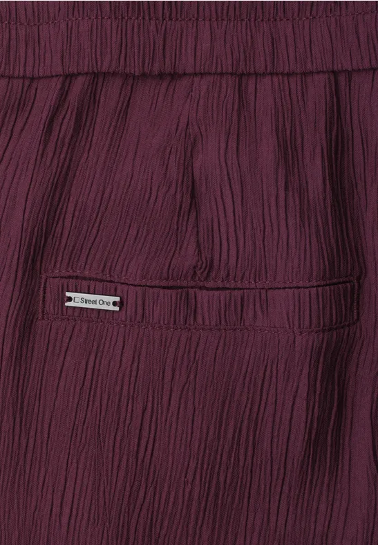 Close-up van een bordeaux gerimpelde broek met achterzak en klein metalen logo