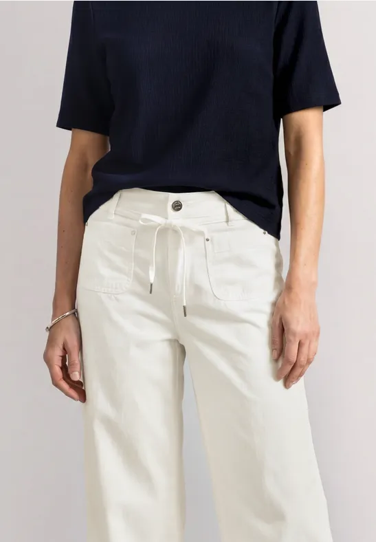 Vrouw in zwart T-shirt met korte mouwen en witte, wijde broek.
