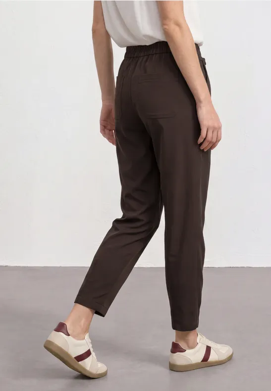 Achteraanzicht van iemand in een casual bruine broek met elastische taille en witte sneakers.
