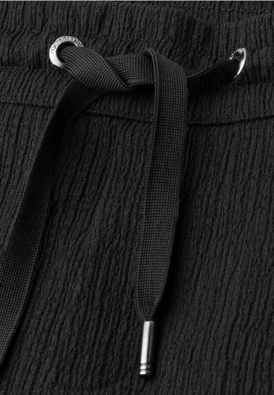 Taille en tissu noir texturé avec cordon élastique et embouts métalliques argentés.
