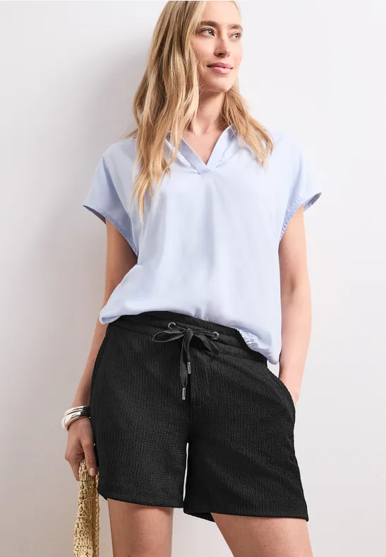 Femme en chemisier bleu pâle, short noir et panier en paille.
