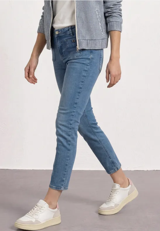 Persoon met blauwe cropped spijkerbroek, witte sneakers en een grijs jasje.