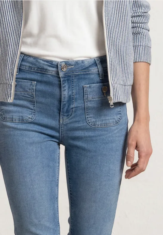 Vrouw in nauwsluitende blauw gemêleerde jeans met opgestikte zakken, wit shirt en gestreepte cardigan.