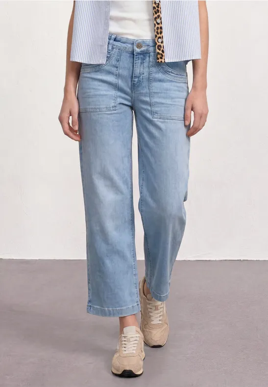jeans bleu clair larges 7/8 portés avec des baskets beige.