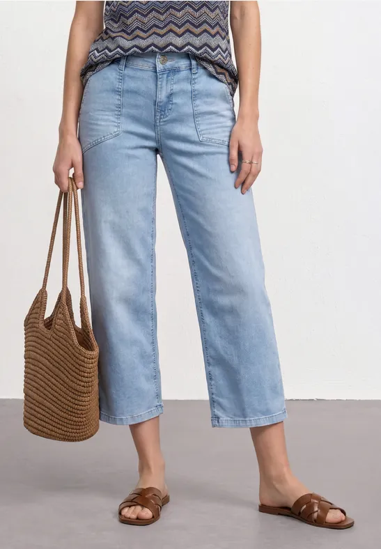 Persoon draagt lichtblauwe, rechte jeans, een gemêleerd topje, een gevlochten tas en gevlochten sandalen.