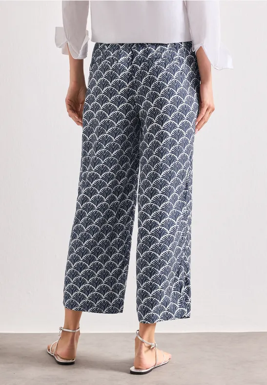 Vue de dos d’une personne en pantalon large bleu à motif blanc, haut blanc et sandales.