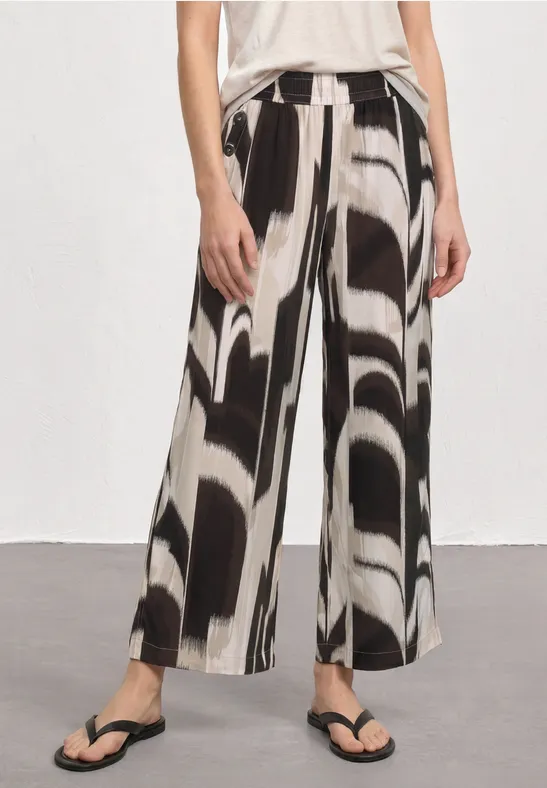 Wijde broek met abstract zwart-wit patroon, gecombineerd met teenslippers.