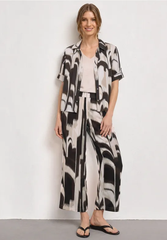 Vrouw draagt een zwart-wit abstract overhemd en losse broek, gecombineerd met wit topje en zwarte sandaal.