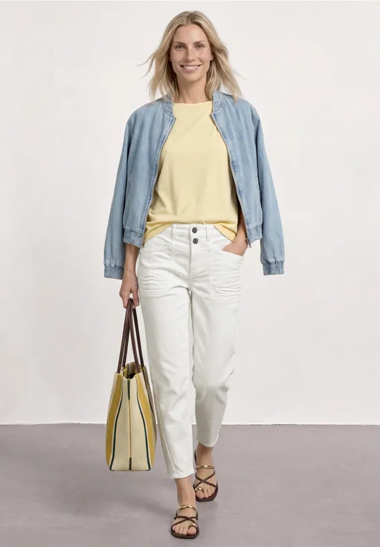 Vrouw in een casual look: lichtblauw jasje, geel shirt, witte broek, sandalen en gele tas.