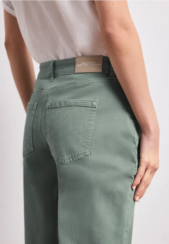 Vue arrière d'une personne portant un jean vert pâle, mains le long des cuisses.