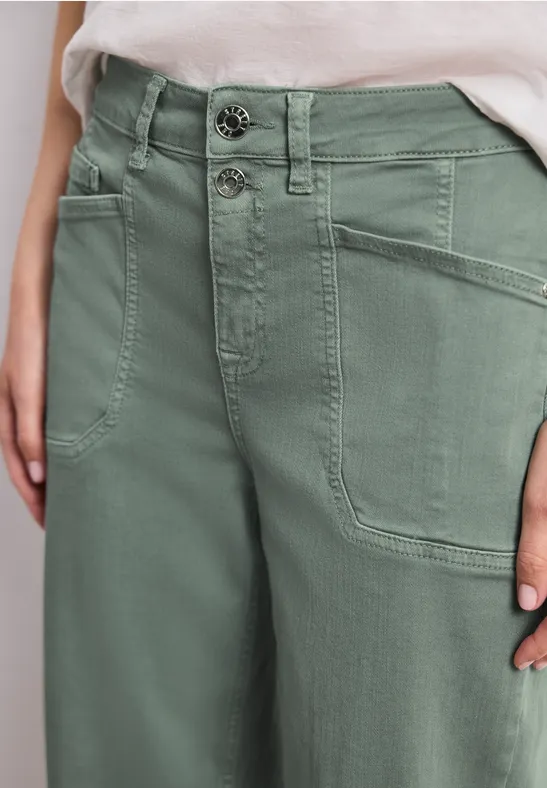 Gros plan sur un pantalon vert olive taille haute, fermeture à double bouton et grandes poches avant.