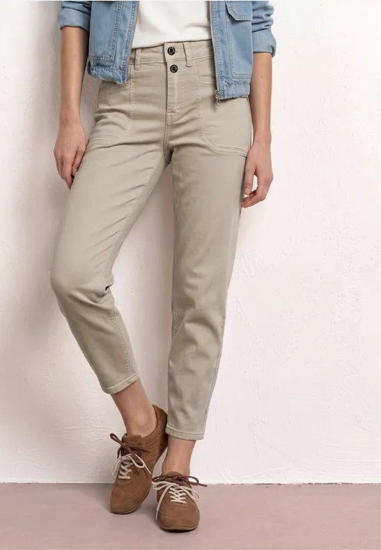 Pantalon beige taille haute à deux boutons, coupe ajustée jusqu'aux chevilles, associé à des chaussures à lacets marron.