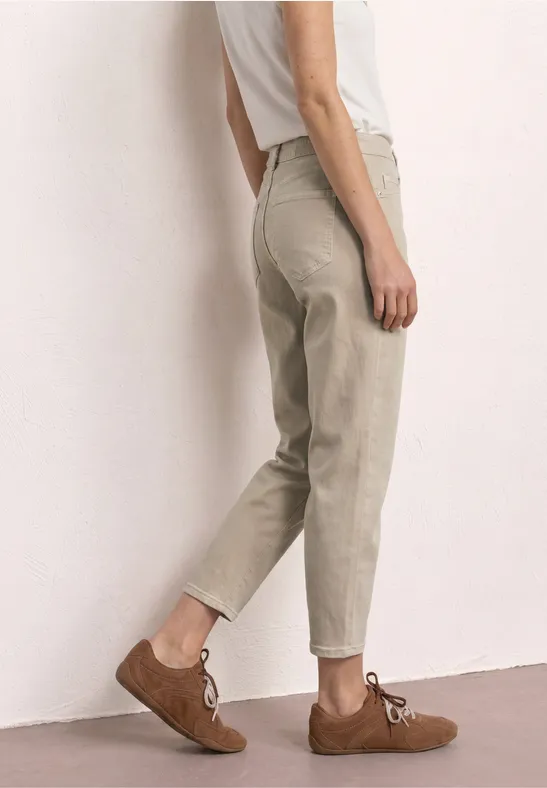 Bas du corps d'une personne portant un pantalon beige ample et des chaussures marron en daim sur fond clair.