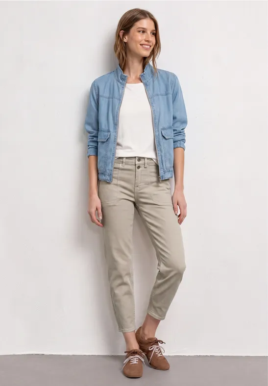 Femme en t-shirt blanc, chemise en jean bleu clair, chinos beiges et chaussures marron sur fond clair.