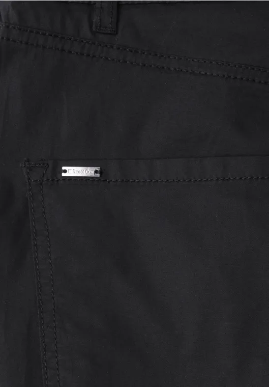 Close-up van een zwarte broek met metalen merkembleem op achterzak.