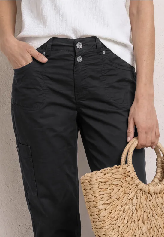 Witte top, zwarte broek met knopen en een gevlochten strooien tas in de hand.
